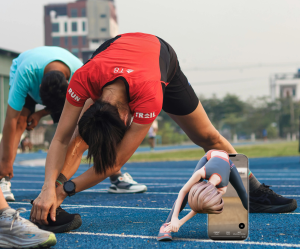 A photo of runners performing standing hamstring stretches during a track warm-up for injury prevention.