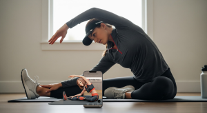 A photo of a woman stretching on a yoga mat indoors with one arm overhead, while a smartphone displaying the WeStretch app is placed in front of her.