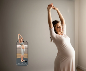 A photo of a pregnant woman stretching her arms overhead near a bright window.