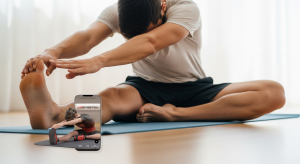 A photo of a man sitting on a yoga mat reaching toward his foot during a seated inner thigh stretch.
