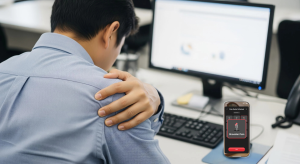 An image of an office worker holding their shoulder due to upper back and shoulder blade pain caused by poor desk posture.