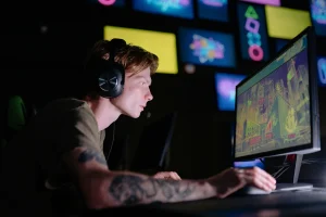 A photo of a gamer wearing a headset and leaning forward toward a computer screen, showing forward head posture and neck strain during gaming.