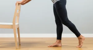 A photo of a heel raise exercise using a chair for balance.