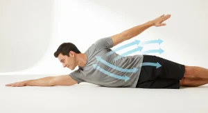 A photo of a man lying on his side with one arm extended and the other reaching back, demonstrating a side-lying chest rotation with blue arrows showing the stretch.