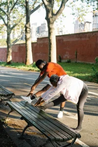 A photo of two people performing hamstring stretches on a park bench as part of energizing morning exercises.