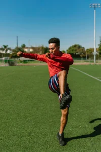 An image of an athlete performing a high kick warm-up exercise on a sports field for injury prevention.