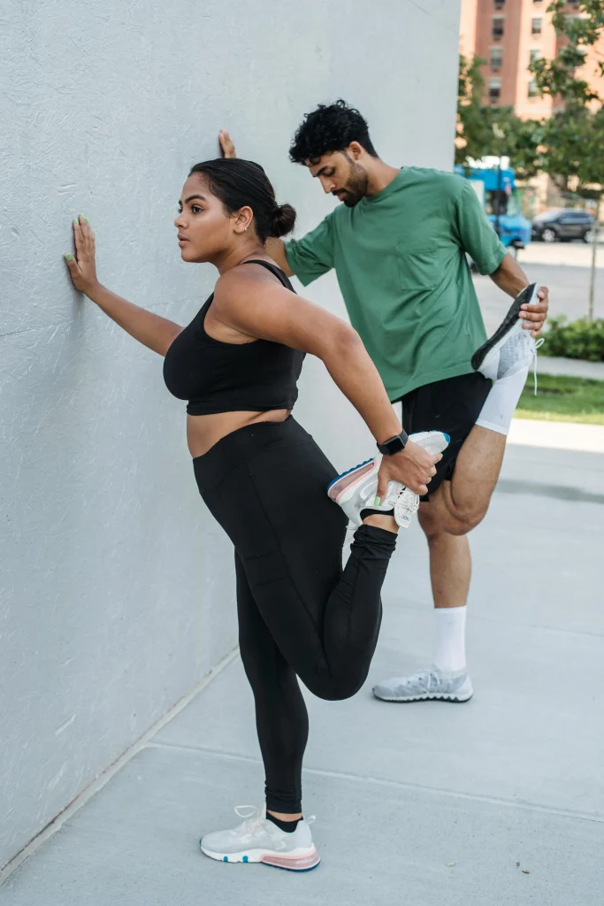 An image of two athletes doing standing quad stretches against a wall as part of cool-down stretches after exercise.
