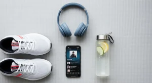An image of workout items on a mat, including running shoes, headphones, a phone with a music playlist, and a water bottle.